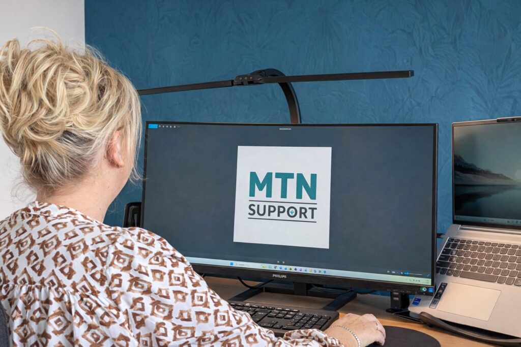 Mirjam, eigenaresse van MTN Support, werkt achter haar bureau terwijl het MTN Support logo zichtbaar is op het scherm.